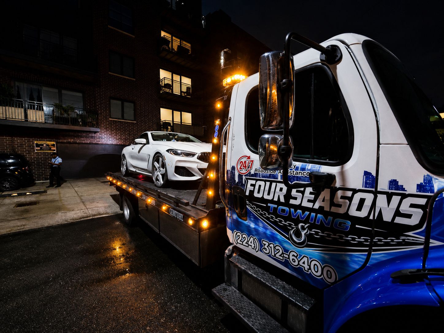 Four Seasons flatbed picking up a car at night in the city